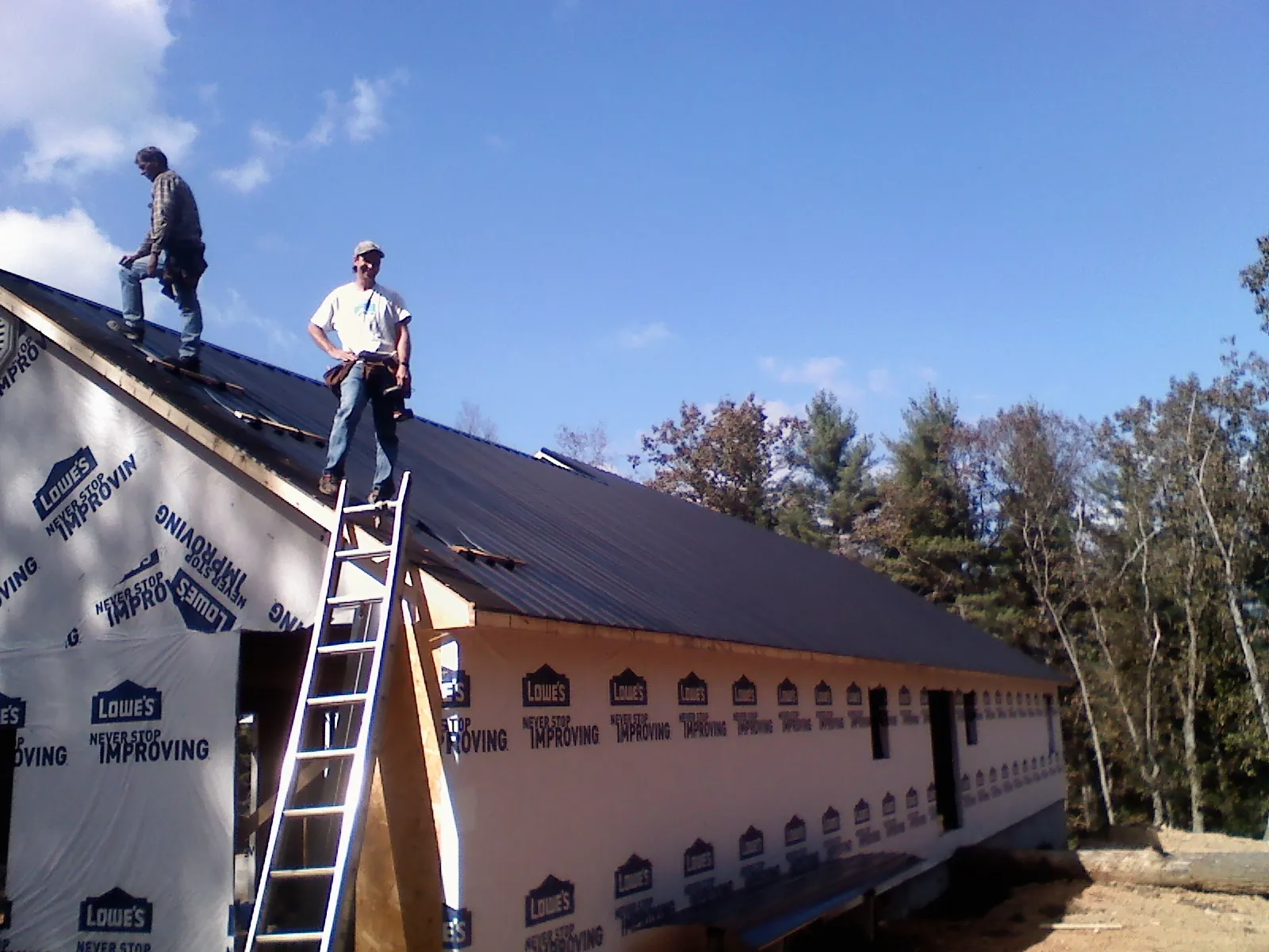 Two roofers standing on a long dark metal roof over a wrapped building in Valparaiso